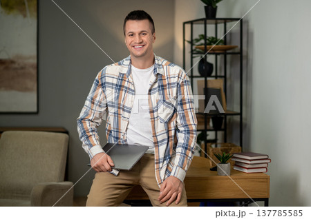 Confident man holding laptop standing in home office interior Confident man holding laptop standing in home office interior 137785585