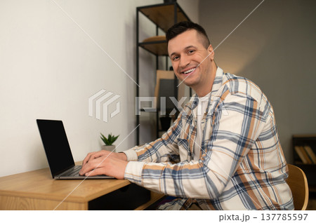 Happy man working on laptop at wooden desk in home office 137785597
