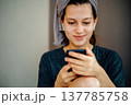 Home portrait of a teen girl with a slight smile and a smartphone in her hands. Earphones and a towel on her head support themes of a pleasant message, communication, music and positive emotion. 137785758