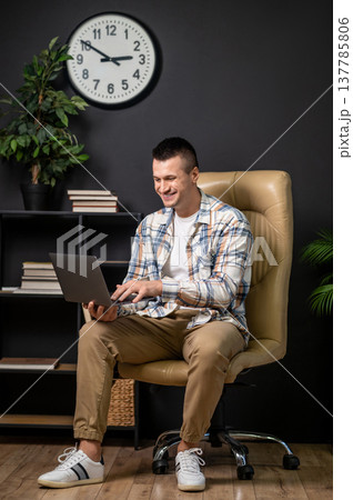Content man using laptop while sitting in office chair in modern interior Content man using laptop while sitting in office chair in modern interior 137785806
