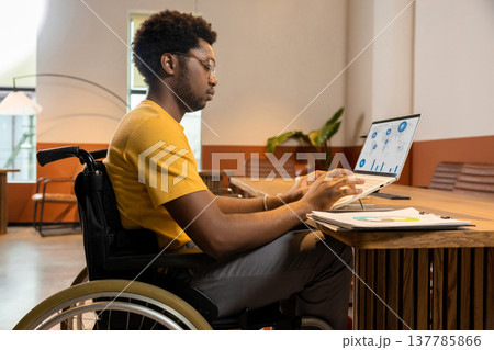 Focused man in wheelchair using laptop working with business data Focused man in wheelchair using laptop working with business data 137785866
