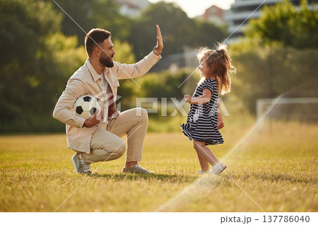 Giving high five, teamwork. Father with his little daughter are on the field Giving high five, teamwork. Father with his little daughter are on the field 137786040