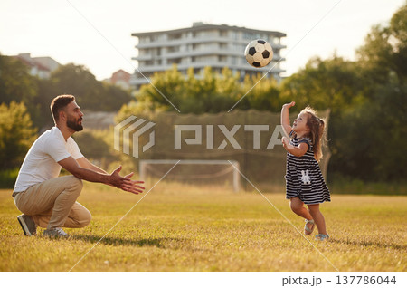 Throwing soccer ball high up. Father with his little daughter are on the field 137786044