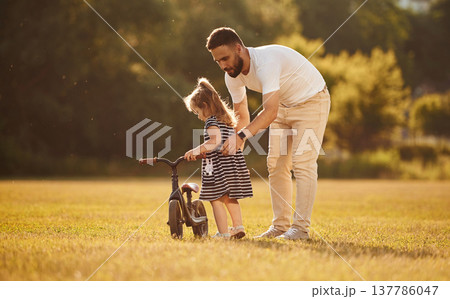With cute little bicycle. Father with his little daughter are on the field 137786047