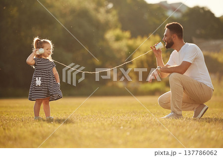 Tin can telephone fun. Father with his little daughter are on the field Tin can telephone fun. Father with his little daughter are on the field 137786062