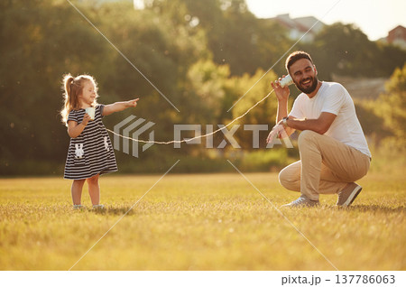 Talking into tin can telephone. Father with his little daughter are on the field 137786063