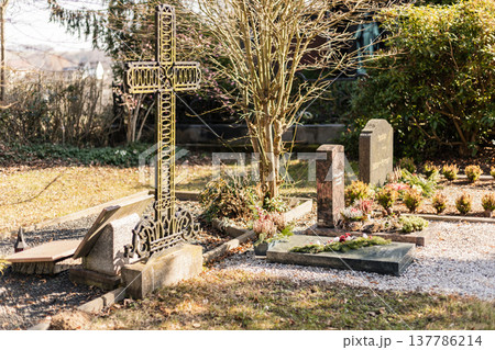 In a cemetery, several gravestones are visible with fresh flowers and decorations. The scene captures a moment of remembrance in broad daylight In a cemetery, several gravestones are visible with fresh flowers and decorations. The scene captures a moment of remembrance in broad daylight 137786214