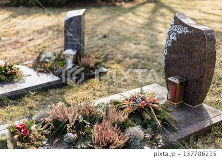 In a cemetery, several gravestones are visible with fresh flowers and decorations. The scene captures a moment of remembrance in broad daylight In a cemetery, several gravestones are visible with fresh flowers and decorations. The scene captures a moment of remembrance in broad daylight 137786215