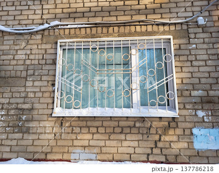 Brick facade with a window with a wrought-iron lattice on a sunny winter day Brick facade with a window with a wrought-iron lattice on a sunny winter day 137786218