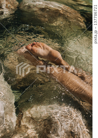 Women's feet in the sea. Close-up top view of a young woman's bare feet in a water. Women's feet in the sea. Close-up top view of a young woman's bare feet in a water. 137786721