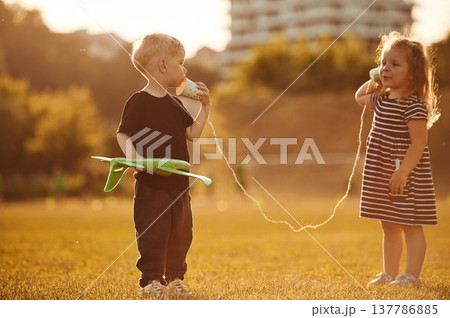 Conversation by using tin can telephone. Two kids are having fun on the summer field Conversation by using tin can telephone. Two kids are having fun on the summer field 137786885