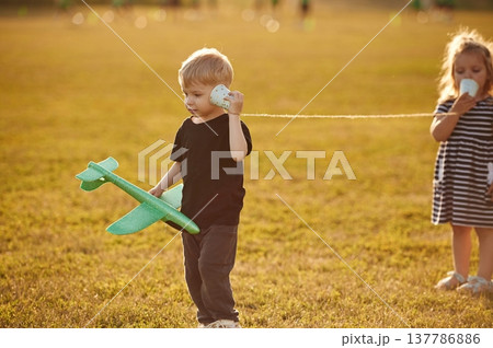Conversation by using tin can telephone. Two kids are having fun on the summer field Conversation by using tin can telephone. Two kids are having fun on the summer field 137786886