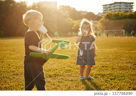 Conversation by using tin can telephone. Two kids are having fun on the summer field Conversation by using tin can telephone. Two kids are having fun on the summer field 137786890