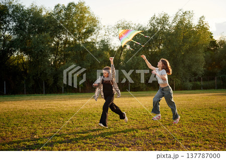 View from the side, running. Two girls kids are playing with kite on the field View from the side, running. Two girls kids are playing with kite on the field 137787000