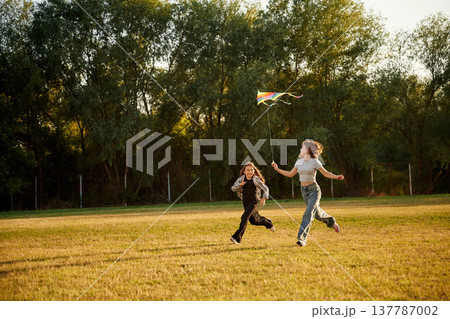View from the side, running. Two girls kids are playing with kite on the field View from the side, running. Two girls kids are playing with kite on the field 137787002