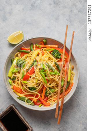 Stir fry wok noodles with vegetables in a plate on a light background with chopsticks, soy sauce Stir fry wok noodles with vegetables in a plate on a light background with chopsticks, soy sauce 137787291