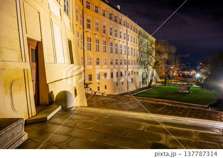 People explore the Garden of Eden at Prague Castle at night. The area shows beautiful outdoor spaces, and the lights highlight the paths and architecture. Visitors enjoy the views of the city. 137787314
