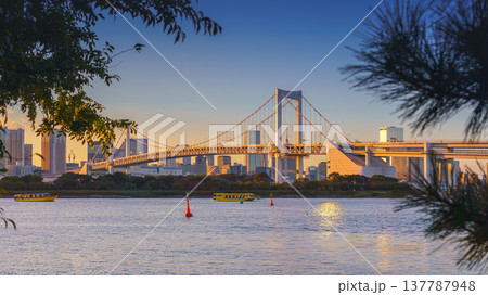 Tokyo, Japan - Oct 13 2024, panoramic view of Tokyo Bay with a cable-stayed Rainbow Bridge above it, a boat and a water bus sailing, at sunset, Tokyo, Japan 137787948