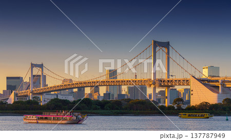 Tokyo, Japan - Oct 13 2024, panoramic view of Tokyo Bay with a cable-stayed Rainbow Bridge above it, a boat and a water bus sailing, at sunset, Tokyo, Japan 137787949
