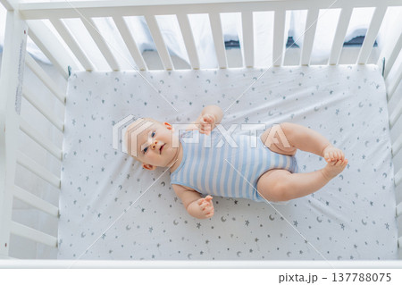 Baby lying peacefully in a cozy crib at home, feeling safe and calm in a warm nursery atmosphere. Simple everyday moment of care and comfort. Infant sleep, early childhood and gentle parenting concept 137788075