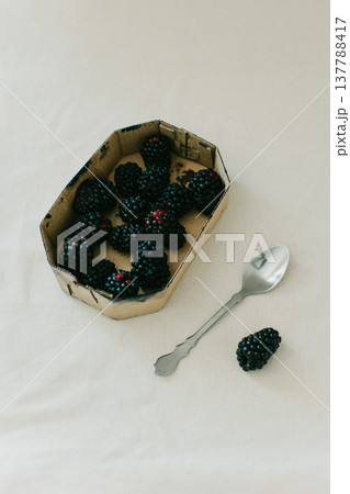 Box with blackberries and a spoon on a light rustic background. Box with blackberries and a spoon on a light rustic background. 137788417