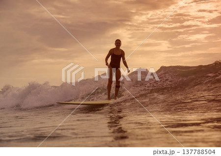 Relaxed Female Rider Gliding On Longboard At Sunset Over Gentle Waters Relaxed Female Rider Gliding On Longboard At Sunset Over Gentle Waters 137788504