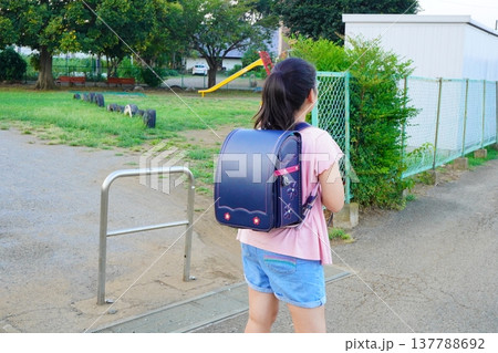ランドセルを背負った小学生の後ろ姿。公園のそばを歩く子どもと通学風景。 ランドセルを背負った小学生の後ろ姿。公園のそばを歩く子どもと通学風景。 137788692