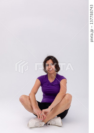 Athlete in comfortable attire seated calmly, Relaxed sports individual tying shoe on studio floor, Serene athlete wearing casual clothing seated on floor with gentle smile Athlete in comfortable attire seated calmly, Relaxed sports individual tying shoe on studio floor, Serene athlete wearing casual clothing seated on floor with gentle smile 137788743