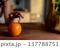 Closeup orange being touched by hand, textural peel emphasized, dim ambient kitchen light, nail polish detail, minimalist table styling, sensory still life composition 137788751