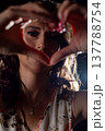 Lowangle woman framing heart symbol, playful expression, rim backlight and sparkling makeup, warm night vibe, shallow focus with grainy film mood, energetic celebratory scene 137788754