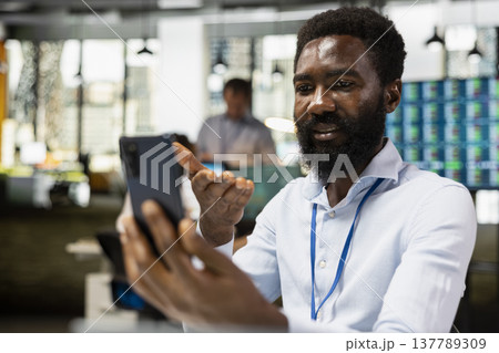 African American male executive using mobile phone for video conference with client, reviewing business plans. Black businessman discussing development goals with partner in virtual meeting. 137789309