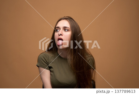 Caucasian woman pulling a funny face and sticking her tongue out on a studio background. Expressing playfulness and humor Caucasian woman pulling a funny face and sticking her tongue out on a studio background. Expressing playfulness and humor 137789613