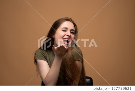 Young woman winking, smiling, and blowing a kiss with a happy, flirty, and playful expression on a brown background 137789621