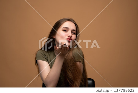 Young woman blowing an air kiss with pursed lips, embodying femininity, charm, and emotional expression 137789622
