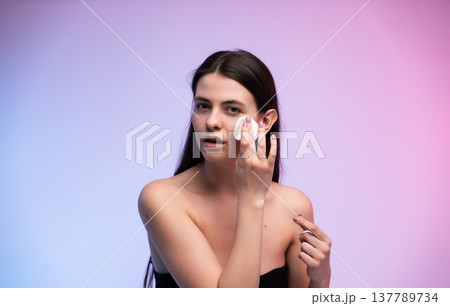 Young woman applying micellar water or toner with a cotton pad to clean her face, emphasizing skincare, beauty, and cosmetic routines for healthy skin 137789734