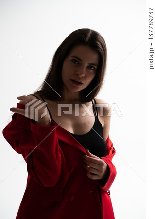 Woman standing in a studio, modeling a red blazer and black camisole, projecting a strong sense of independence and stylish composure against a white background Woman standing in a studio, modeling a red blazer and black camisole, projecting a strong sense of independence and stylish composure against a white background 137789737