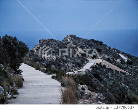 Serene Coastal Mountain Trail Winding Past Rocks And Sparse Vegetation Under Bright Blue Sky Serene Coastal Mountain Trail Winding Past Rocks And Sparse Vegetation Under Bright Blue Sky 137790537