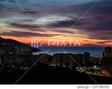 Serene Evening View, Gentle Nightfall By Sea With Distant Mountains And Shimmering Water Reflections 137790703