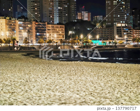 Beach Lights Sparkle, Silvery Reflections Dance On Sand Beneath Distant Skyscrapers And Gentle Sea Movements Beach Lights Sparkle, Silvery Reflections Dance On Sand Beneath Distant Skyscrapers And Gentle Sea Movements 137790717
