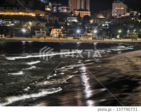 Coastal Night Scene, Shining Shoreline With City Lights, Reflective Waves Illuminate Nighttime Waterfront 137790731