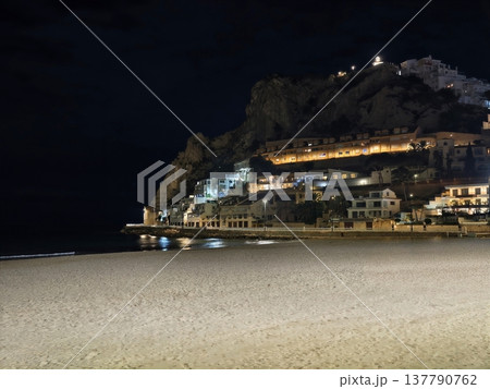 Serene Seaside Scene, Tranquil Nighttime Beachscape Showcasing Luminous Town Against Rocky Cliffs Serene Seaside Scene, Tranquil Nighttime Beachscape Showcasing Luminous Town Against Rocky Cliffs 137790762
