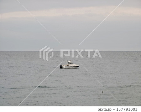 Isolated Vessel On Peaceful Water, Single Motorized Boat Drifting In Calm Grey Ocean Beneath Cloudy Sky 137791003