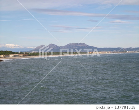 Serene Coast With Distant Hills, Expansive Sandy Beach Beneath Pale Blue Sky And Distant Peaks 137791319