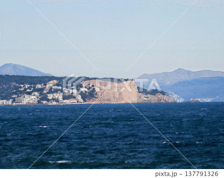 Seaside Cliff View, Edge Of Island With Rough Waters And Structures Silhouetted Against Light Sky 137791326