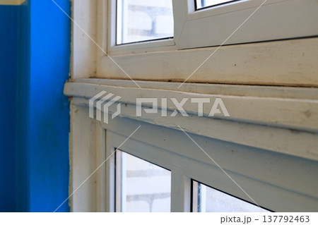Close-up worn white window frame with visible signs of aging and peeling paint next to bright blue wall 137792463