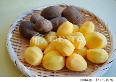 皮付きのじゃがいもと皮をむいたじゃがいもを竹ざるに並べた料理準備の食材写真。 皮付きのじゃがいもと皮をむいたじゃがいもを竹ざるに並べた料理準備の食材写真。 137794070