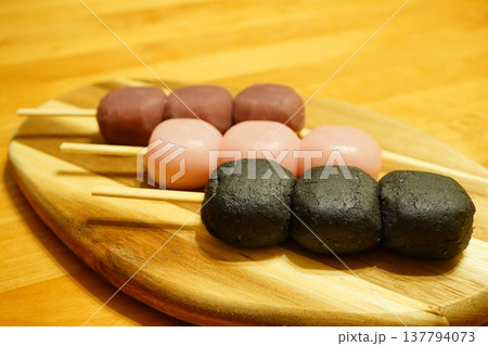 木製プレートに並べた三色団子と黒ごま団子の和菓子写真。日本の伝統的な串団子を並べた甘味のイメージ素材 137794073
