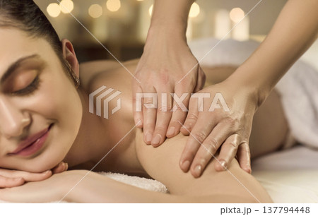 Relaxed woman receiving shoulder massage in spa with warm candlelight ambience 137794448