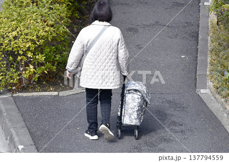 日本の横浜都市景観カートの高齢女性(マスク姿)、段差や隙間でカートはガタガタ揺れ歩きにくい…人生とは 137794559