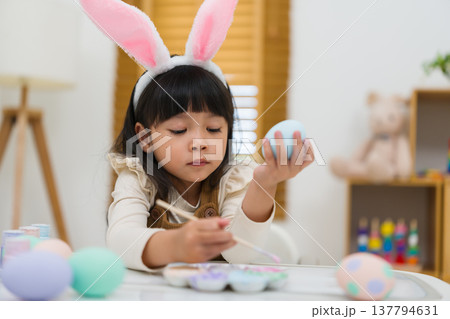 preschool child girl wearing bunny ears painting and decorating colorful egg at home on easter day preschool child girl wearing bunny ears painting and decorating colorful egg at home on easter day 137794631